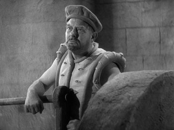 Movie still from “The Private Life of Henry VIII” (1933), directed by Alexander Korda – Black and white photograph of a statue of a man holding a hammer; Medium shot, High angle