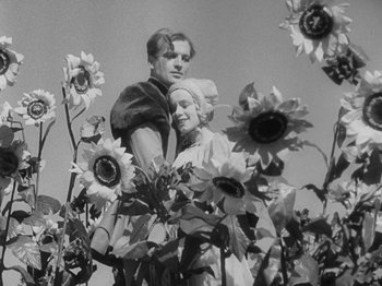 Movie still from “The Private Life of Henry VIII” (1933), directed by Alexander Korda – A man and a woman standing next to a field of sunflowers; Medium shot, Low angle