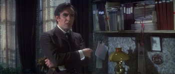 Movie still from “The Private Life of Sherlock Holmes” (1970), directed by Billy Wilder – A man in a suit and tie standing in front of a lamp; Medium shot, Over the shoulder angle
