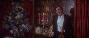 Movie still from “The Private Life of Sherlock Holmes” (1970), directed by Billy Wilder – A man in a tuxedo holding a violin in front of candles; Medium shot, High angle
