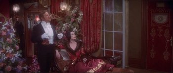 Movie still from “The Private Life of Sherlock Holmes” (1970), directed by Billy Wilder – A woman sitting on top of a couch wearing a red dress; Medium shot, High angle