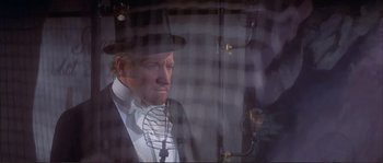 Movie still from “The Private Life of Sherlock Holmes” (1970), directed by Billy Wilder – A man wearing a top hat and holding a microphone; Medium shot, Over the shoulder angle