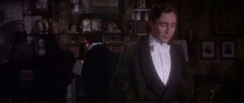 Movie still from “The Private Life of Sherlock Holmes” (1970), directed by Billy Wilder – A man in a tuxedo standing in front of a bookshelf; Medium shot, Over the shoulder angle