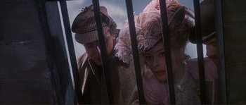 Movie still from “The Private Life of Sherlock Holmes” (1970), directed by Billy Wilder – A man and a woman wearing hats looking through a fence; Close Up shot, Low angle