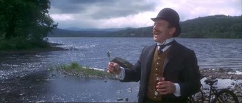 Movie still from “The Private Life of Sherlock Holmes” (1970), directed by Billy Wilder – A man in a suit and a hat holding a fork and a drink; Medium shot, Low angle