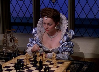 Movie still from “The Private Lives of Elizabeth and Essex” (1939), directed by Michael Curtiz – A woman dressed in period clothing playing a game of chess; Close Up shot, High angle
