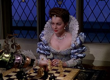 Movie still from “The Private Lives of Elizabeth and Essex” (1939), directed by Michael Curtiz – A woman dressed in period clothing playing a game of chess; Medium shot, Over the shoulder angle
