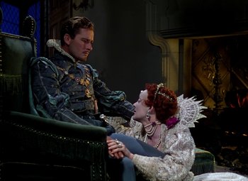 Movie still from “The Private Lives of Elizabeth and Essex” (1939), directed by Michael Curtiz – A man and a woman sitting on top of a couch; Medium shot, Low angle