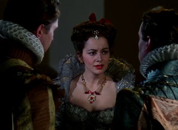 Movie still from “The Private Lives of Elizabeth and Essex” (1939), directed by Michael Curtiz – A woman wearing a red necklace and a black and white dress; Close Up shot, Over the shoulder angle