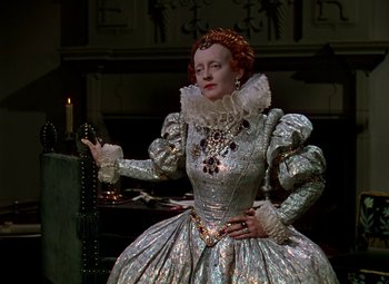 Movie still from “The Private Lives of Elizabeth and Essex” (1939), directed by Michael Curtiz – A woman dressed in a silver dress holding a candle; Medium shot, Low angle