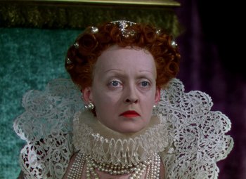 Movie still from “The Private Lives of Elizabeth and Essex” (1939), directed by Michael Curtiz – An older woman with red hair wearing a white dress and pearls; Close Up shot, High angle