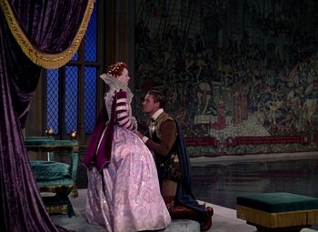 Movie still from “The Private Lives of Elizabeth and Essex” (1939), directed by Michael Curtiz – A man kneeling down next to a woman dressed in medieval garb; Wide shot, High angle