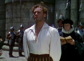 Movie still from “The Private Lives of Elizabeth and Essex” (1939), directed by Michael Curtiz – A man wearing a white shirt and a black and gold skirt; Medium shot, Low angle