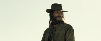 Movie still from “The Proposition” (2005), directed by John Hillcoat – A man with long hair wearing a hat and a suit; Close Up shot, Low angle