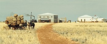 Movie still from “The Proposition” (2005), directed by John Hillcoat – A dirt road leading to an old building in the middle of a field; Extreme Wide shot, Low angle