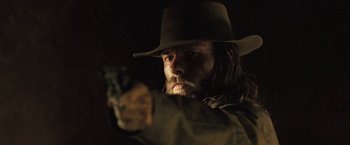 Movie still from “The Proposition” (2005), directed by John Hillcoat – A man in a hat is holding a gun; Close Up shot, Low angle