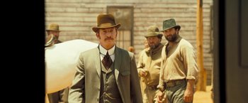 Movie still from “The Proposition” (2005), directed by John Hillcoat – A man in a suit and hat standing next to two other men; Medium shot, Low angle