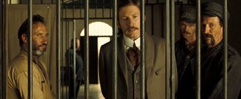 Movie still from “The Proposition” (2005), directed by John Hillcoat – A man standing behind bars in a jail cell; Medium shot, Low angle