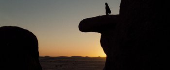 Movie still from “The Proposition” (2005), directed by John Hillcoat – A person standing on top of a rock at sunset; Extreme Wide shot, Low angle