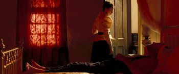 Movie still from “The Proposition” (2005), directed by John Hillcoat – A woman standing in front of a bed in a room; Wide shot, Low angle