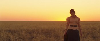 Movie still from “The Proposition” (2005), directed by John Hillcoat – A woman standing in the middle of an open field at sunset; Extreme Wide shot, Low angle