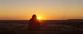 Movie still from “The Proposition” (2005), directed by John Hillcoat – A person sitting in the sand looking at the sunset; Extreme Wide shot, Low angle
