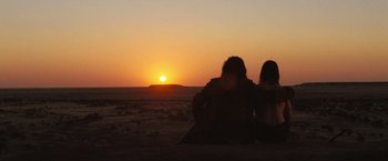 Movie still from “The Proposition” (2005), directed by John Hillcoat – Two people sitting on a bench watching the sun go down; Wide shot, Over the shoulder angle