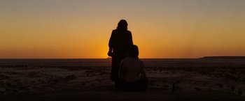 Movie still from “The Proposition” (2005), directed by John Hillcoat – Two people sitting on the beach watching the sun go down; Wide shot, Over the shoulder angle