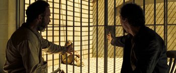 Movie still from “The Proposition” (2005), directed by John Hillcoat – Two people are in a jail cell , one of which is holding his hand out; Wide shot, High angle