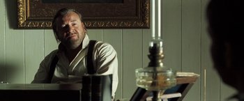 Movie still from “The Proposition” (2005), directed by John Hillcoat – A man sitting in front of a table with a candle; Medium shot, Over the shoulder angle