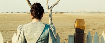 Movie still from “The Proposition” (2005), directed by John Hillcoat – A woman standing next to a tree in the middle of the desert; Wide shot, Over the shoulder angle