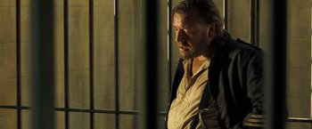 Movie still from “The Proposition” (2005), directed by John Hillcoat – A man standing in front of a metal fence; Close Up shot, Over the shoulder angle