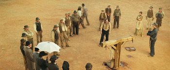 Movie still from “The Proposition” (2005), directed by John Hillcoat – A group of men standing in a dirt field; Wide shot, High angle