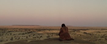 Movie still from “The Proposition” (2005), directed by John Hillcoat – A woman sitting on the ground in the middle of a desert; Extreme Wide shot, High angle