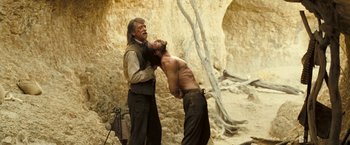 Movie still from “The Proposition” (2005), directed by John Hillcoat – A man is shaving another man's face outside; Medium shot, Over the shoulder angle
