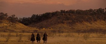 Movie still from “The Proposition” (2005), directed by John Hillcoat – Three people riding horses in a field at sunset; Extreme Wide shot, Low angle
