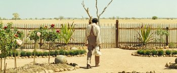 Movie still from “The Proposition” (2005), directed by John Hillcoat – A man walking in a field with a bag of food; Wide shot, Over the shoulder angle