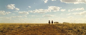 Movie still from “The Proposition” (2005), directed by John Hillcoat – Two people riding horses on a dirt field; Extreme Wide shot, Low angle