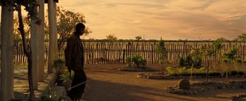 Movie still from “The Proposition” (2005), directed by John Hillcoat – A man walking on a dirt path near a fence; Extreme Wide shot, Over the shoulder angle
