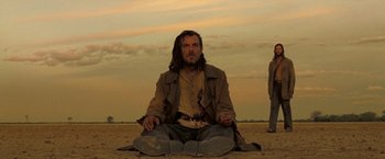 Movie still from “The Proposition” (2005), directed by John Hillcoat – A man sitting on the ground in the desert; Wide shot, Low angle