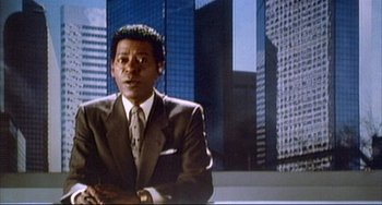Movie still from “The Punisher” (1989), directed by Mark Goldblatt – A man wearing a suit and tie in front of some buildings; Medium shot, Low angle