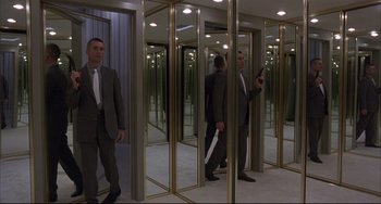 Movie still from “The Punisher” (1989), directed by Mark Goldblatt – A man in a suit and tie holding a knife in front of a mirror; Wide shot, Low angle