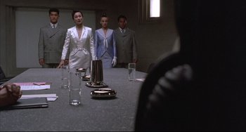 Movie still from “The Punisher” (1989), directed by Mark Goldblatt – A group of people standing around a long table; Medium shot, Over the shoulder angle