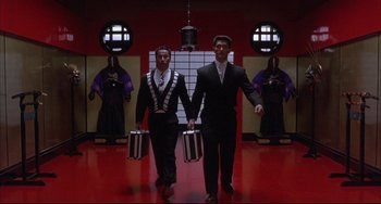 Movie still from “The Punisher” (1989), directed by Mark Goldblatt – A couple of men walking down a red floor holding suitcases; Wide shot, Low angle