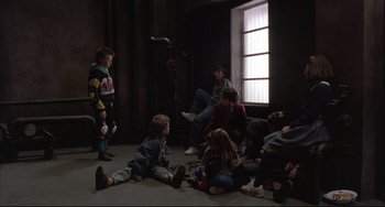 Movie still from “The Punisher” (1989), directed by Mark Goldblatt – A group of people sitting on the floor in a room; Wide shot, High angle