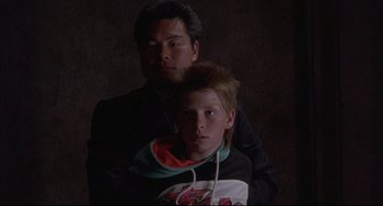 Movie still from “The Punisher” (1989), directed by Mark Goldblatt – A man standing next to a young boy in a dark room; Close Up shot, Low angle