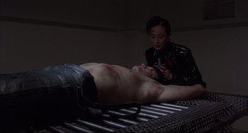 Movie still from “The Punisher” (1989), directed by Mark Goldblatt – A man is laying on a bed while a woman looks at him; Medium shot, Low angle
