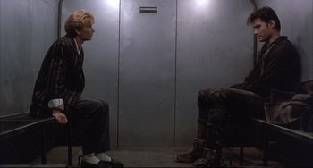 Movie still from “The Punisher” (1989), directed by Mark Goldblatt – A woman sitting on a chair next to a door; Wide shot, Low angle