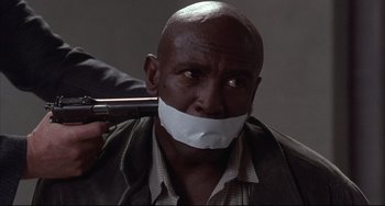 Movie still from “The Punisher” (1989), directed by Mark Goldblatt – A man with a gun and tape over his mouth; Close Up shot, Over the shoulder angle
