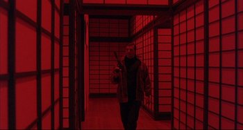 Movie still from “The Punisher” (1989), directed by Mark Goldblatt – A man holding a gun walking in a room with red lighting; Wide shot, Low angle